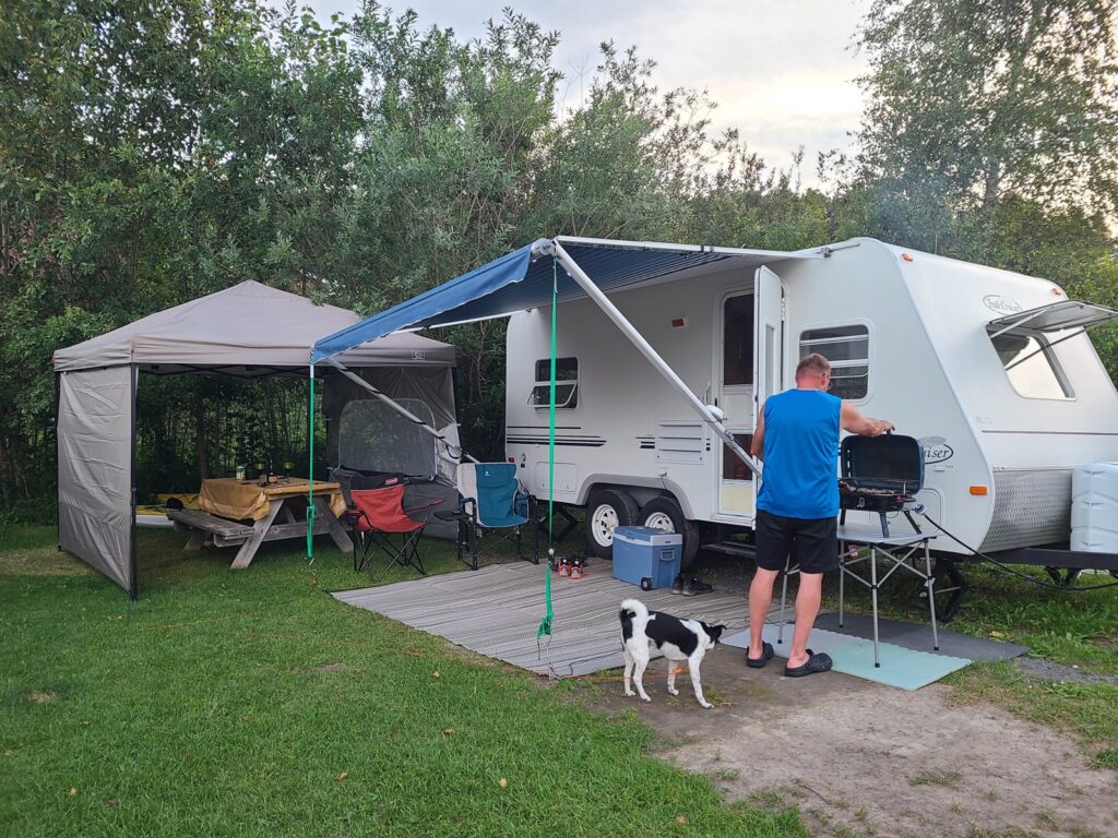 Notre roulotte, l’abri et la table à notre emplacement, avec Christian au barbecue et Shiro