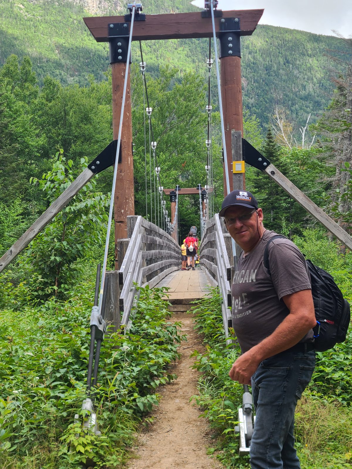 Christian devant le pont suspendu du sentier Le Riverain
